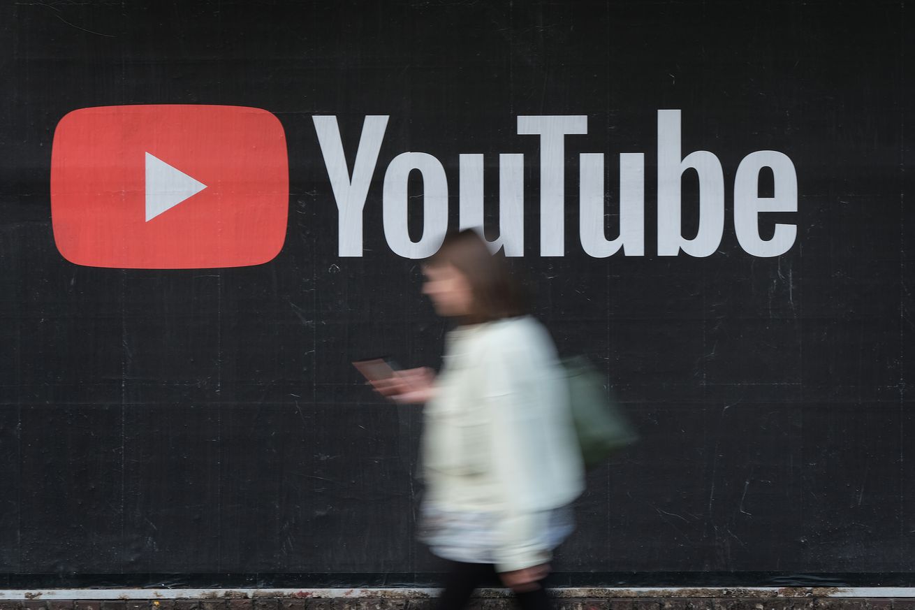 A woman looks down at her phone while walking past a billboard with the YouTube logo.